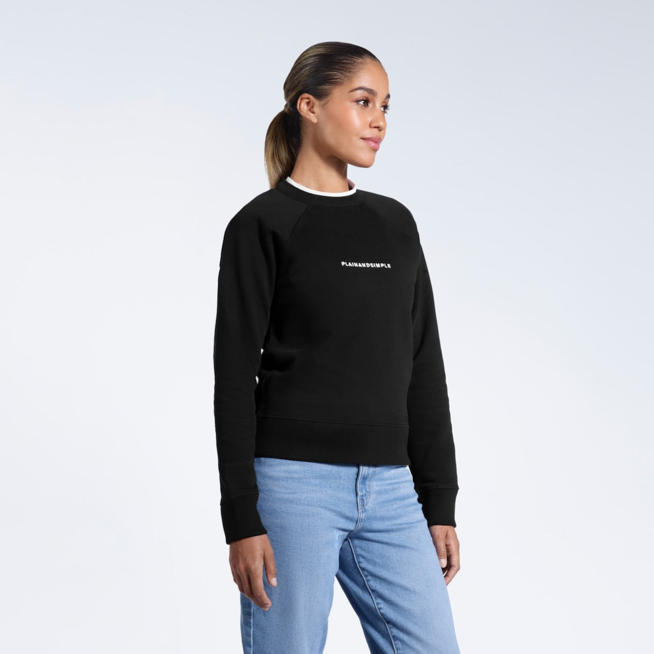 A woman looking away from the camera with her arms by her sides, modelling a branded black heavyweight organic cotton sweatshirt.