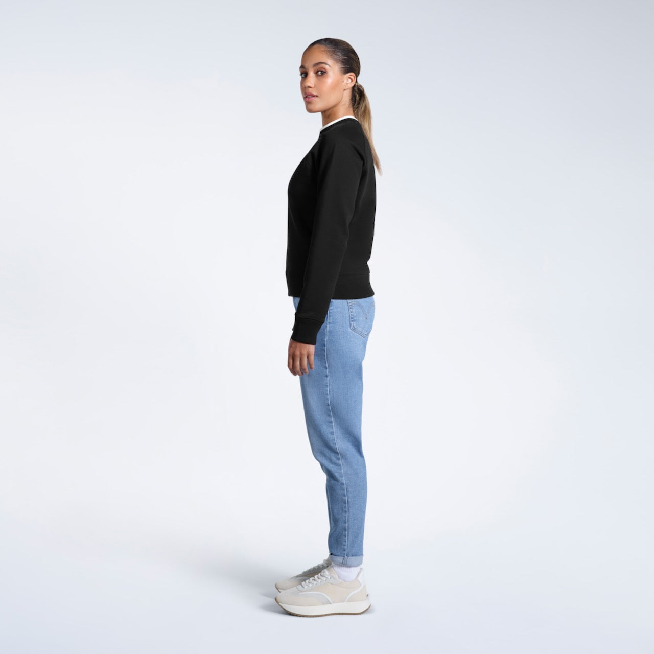 A full body photo of a woman side on looking back at the camera, modelling a black heavyweight organic cotton sweatshirt.