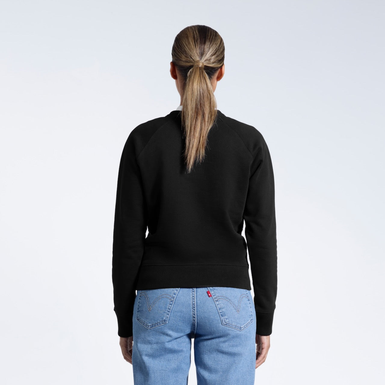 A woman facing away from the camera, showing the back of her black heavyweight organic cotton sweatshirt.