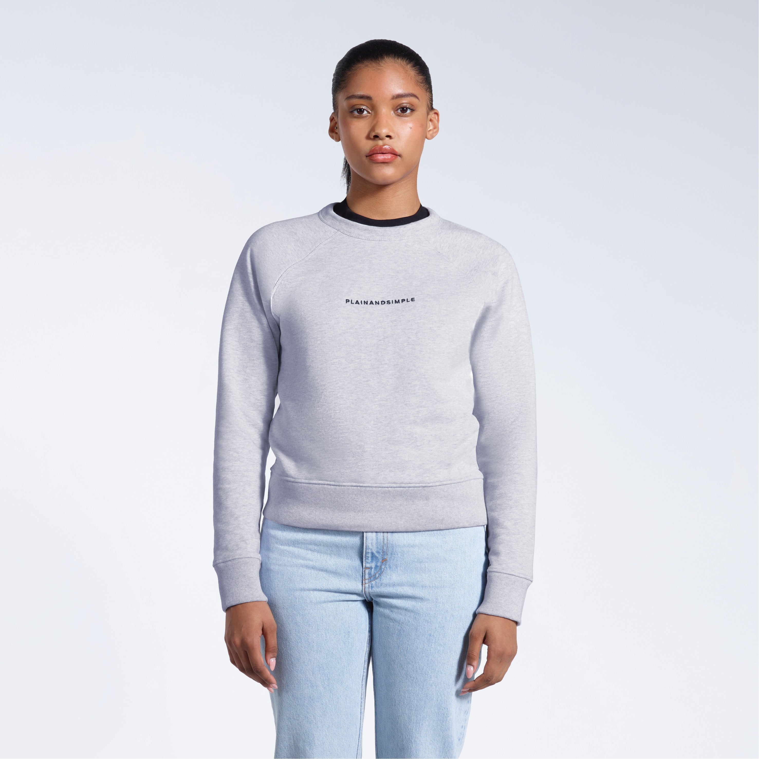 A woman face on with her arms by her side, modelling a branded grey heavyweight organic cotton sweatshirt.