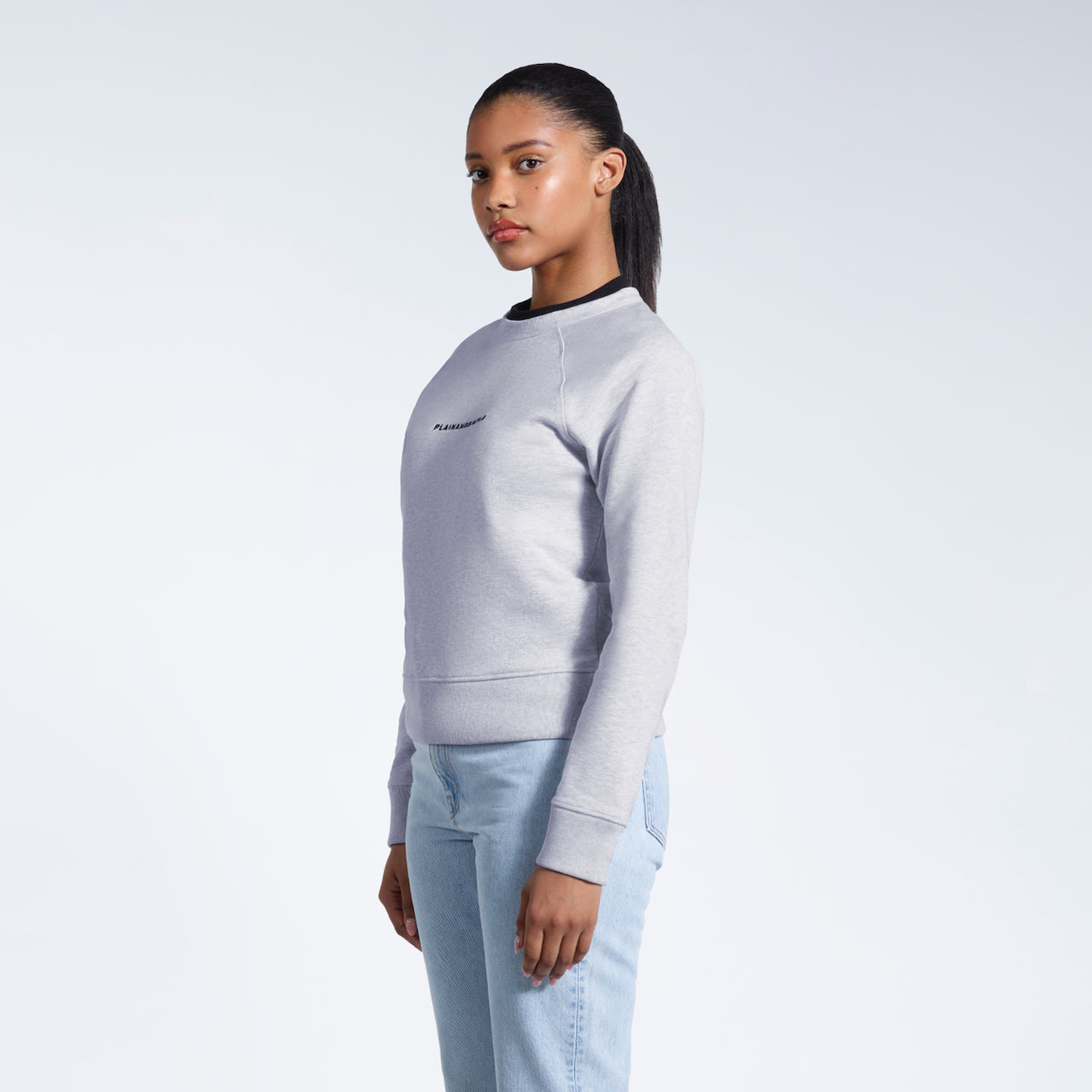 A woman looking into the camera, modelling a grey branded heavyweight organic cotton sweatshirt.