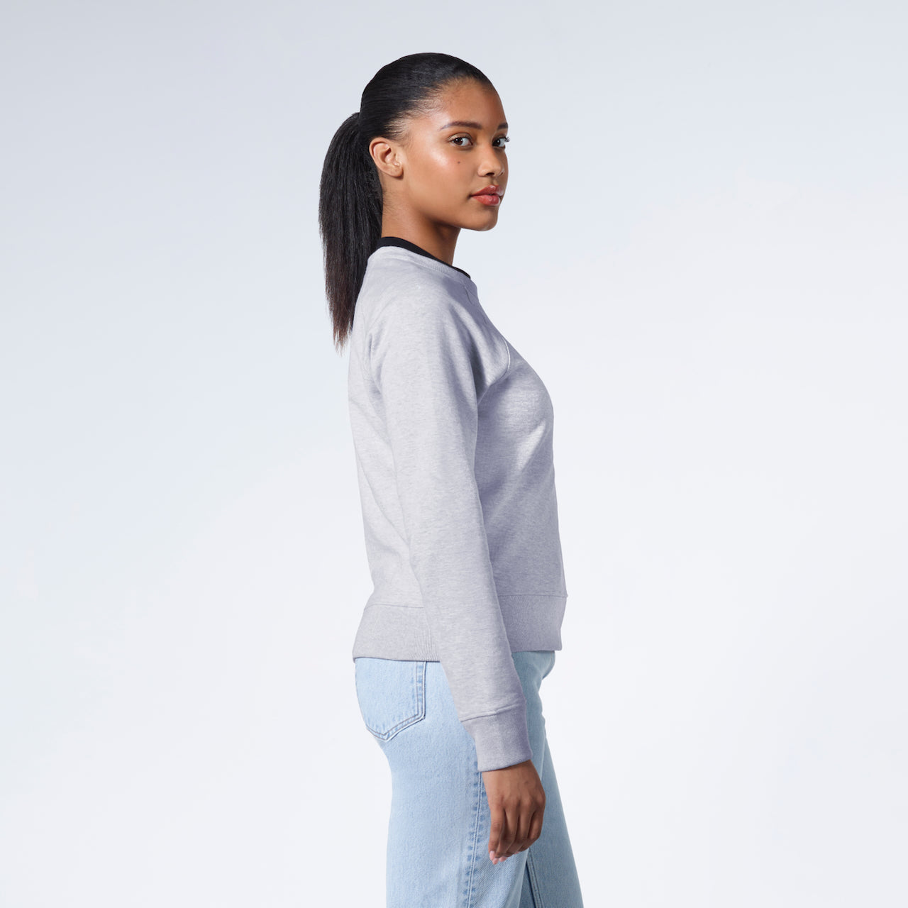 A woman side on looking back at the camera, modelling a grey heavyweight organic cotton sweatshirt.