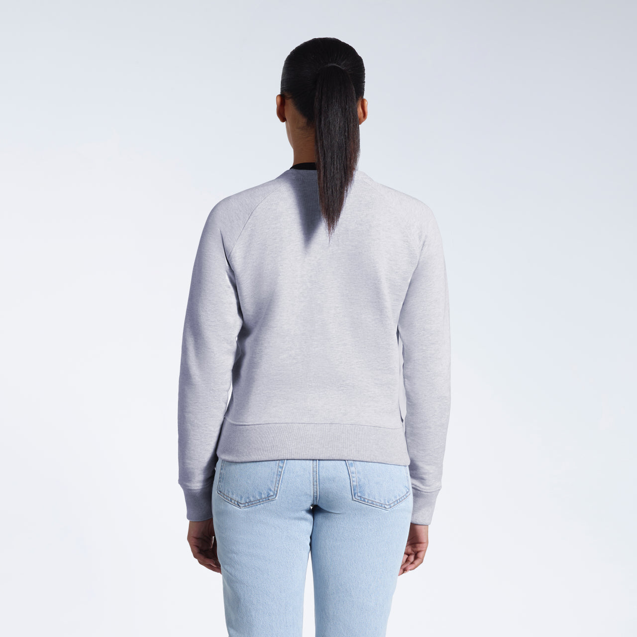 A woman facing away from the camera, showing the back of her grey heavyweight organic cotton sweatshirt.