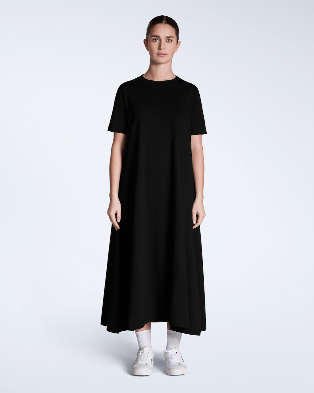 A woman facing front on with her arms by her side, modelling a plain black, long line, maxi organic cotton t shirt dress.