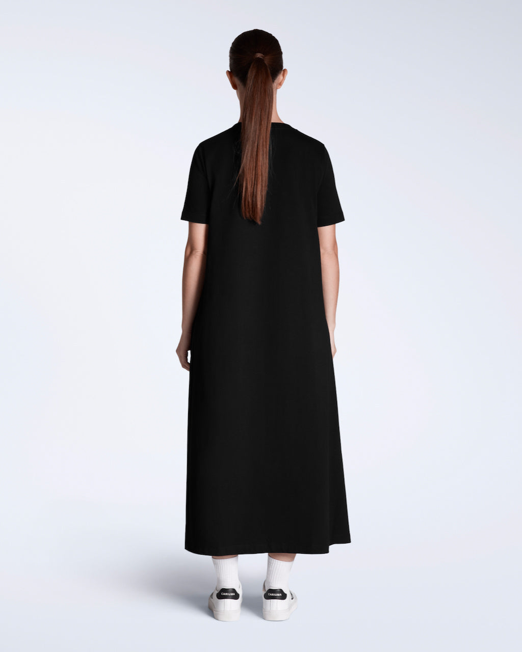 A woman facing away from the camera, modelling a plain black, long line, maxi organic cotton t shirt dress.