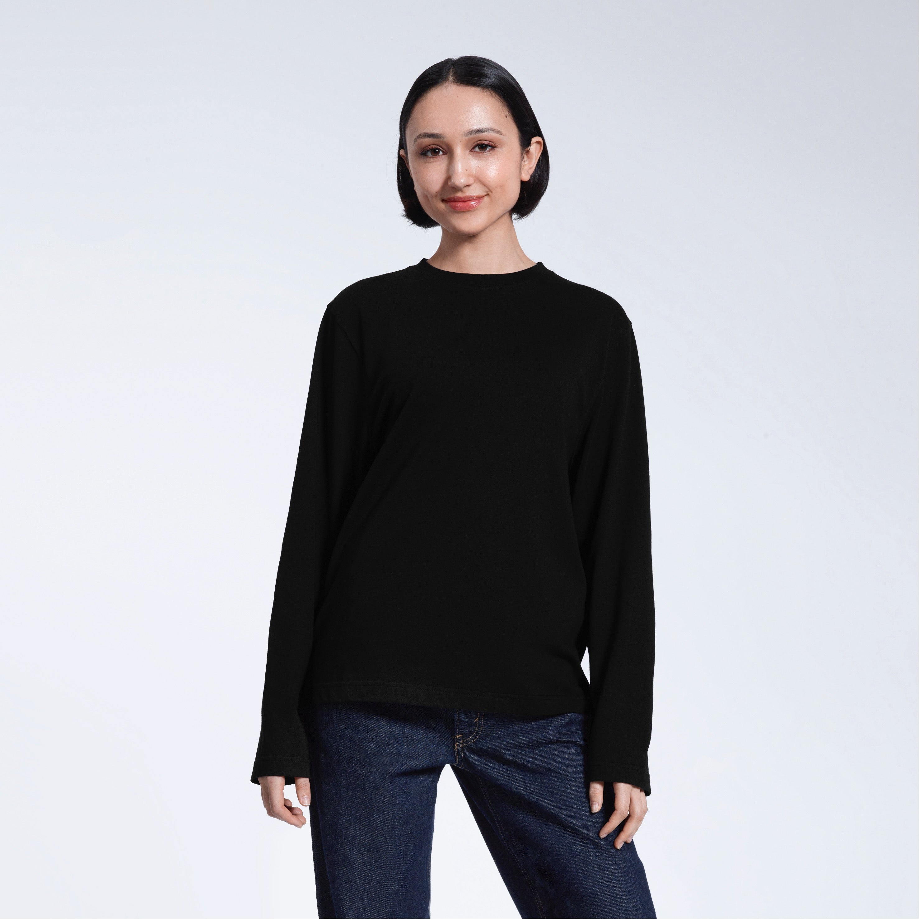 A woman standing front on with her arms by her sides, modelling a plain black long sleeve organic cotton t shirt.