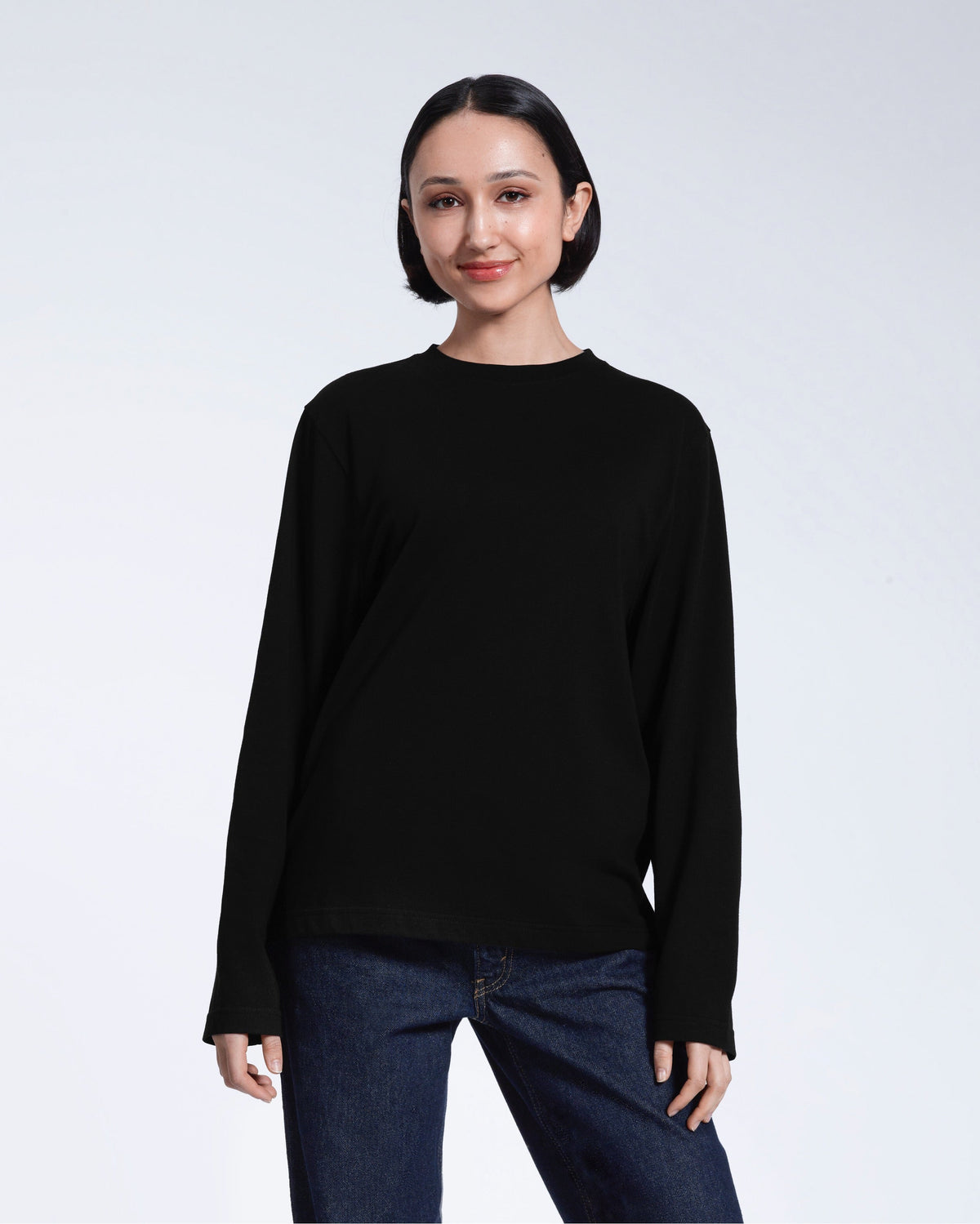 A woman standing front on with her arms by her sides, modelling a plain black long sleeve organic cotton t shirt.