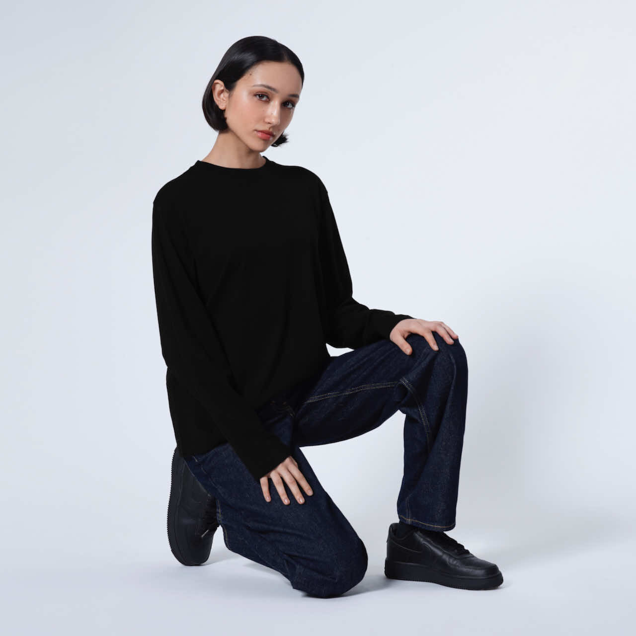 A woman kneeling down looking into the camera, modelling a plain black long sleeve organic cotton t shirt.