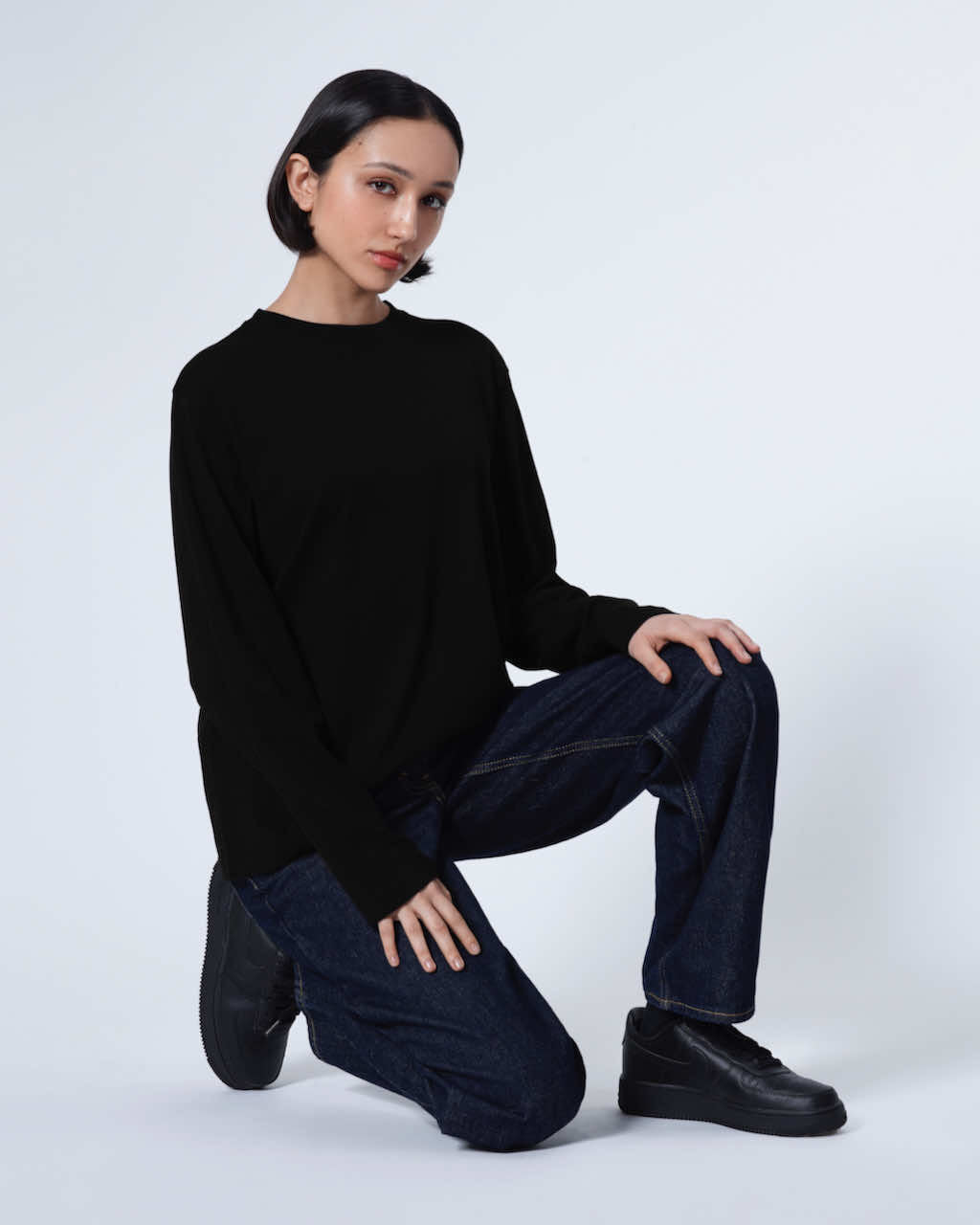 A woman kneeling down looking into the camera, modelling a plain black long sleeve organic cotton t shirt.
