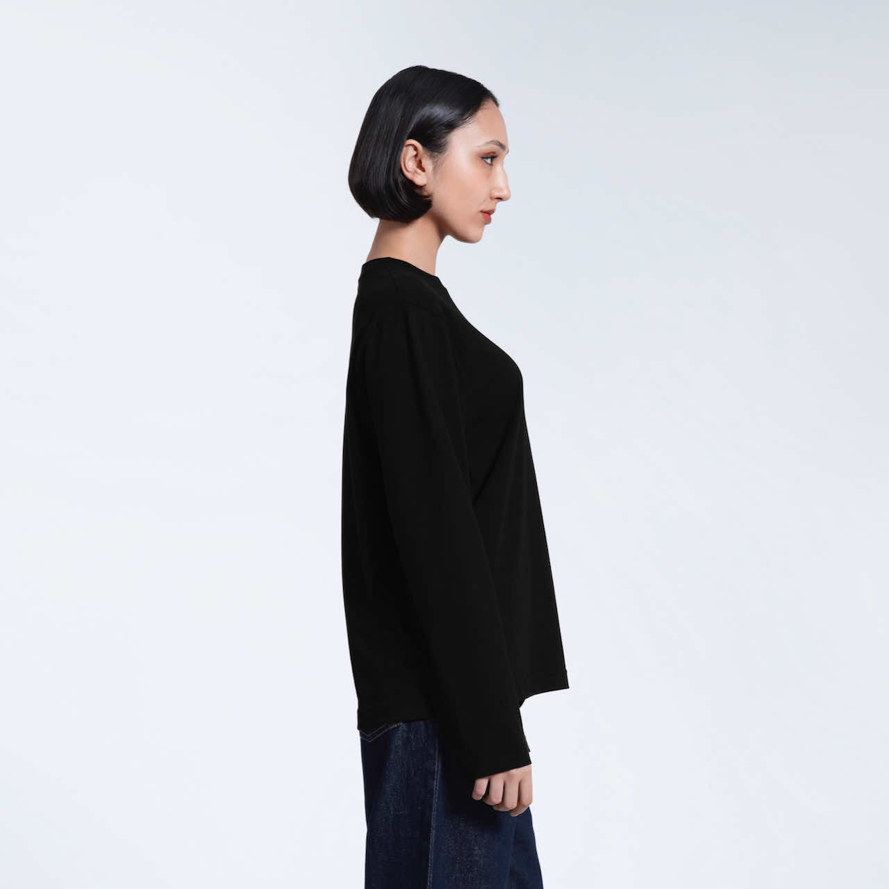 A woman facing side on with her arms by her sides, modelling a plain black long sleeve organic cotton t shirt.