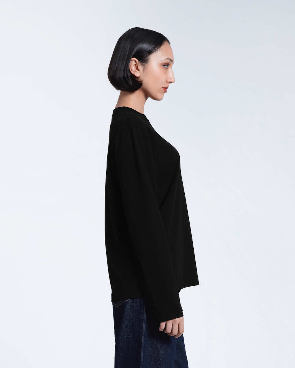 A woman facing side on with her arms by her sides, modelling a plain black long sleeve organic cotton t shirt.