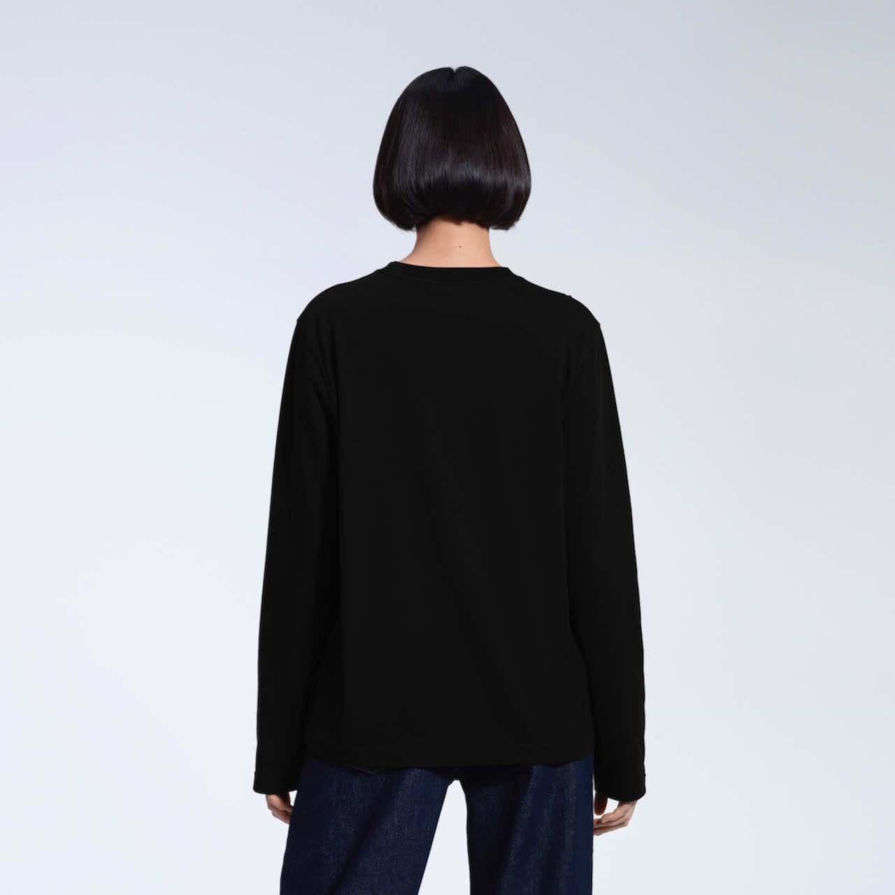 A woman facing away from the camera with her arms by her sides, modelling a plain black long sleeve organic cotton t shirt.
