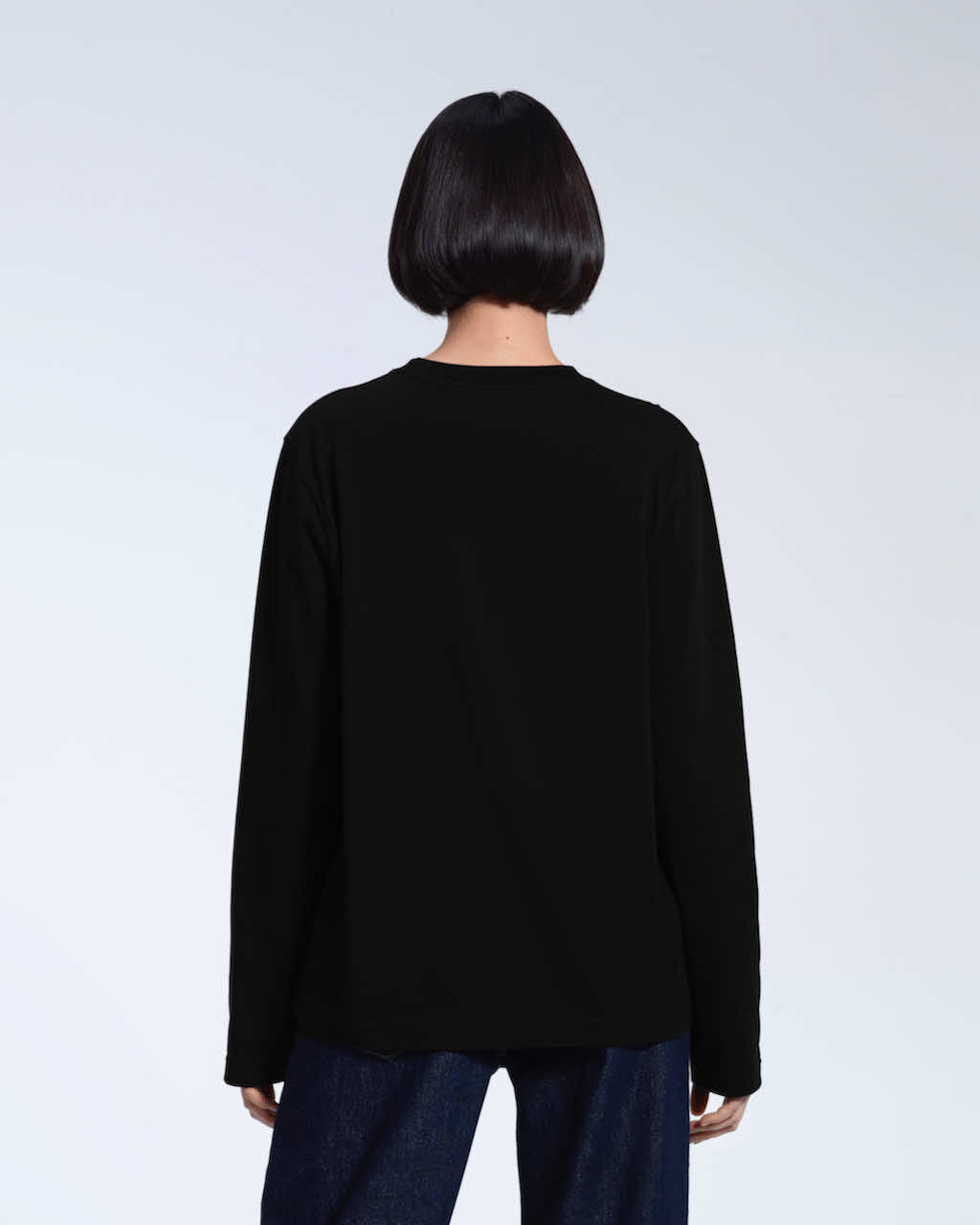 A woman facing away from the camera with her arms by her sides, modelling a plain black long sleeve organic cotton t shirt.