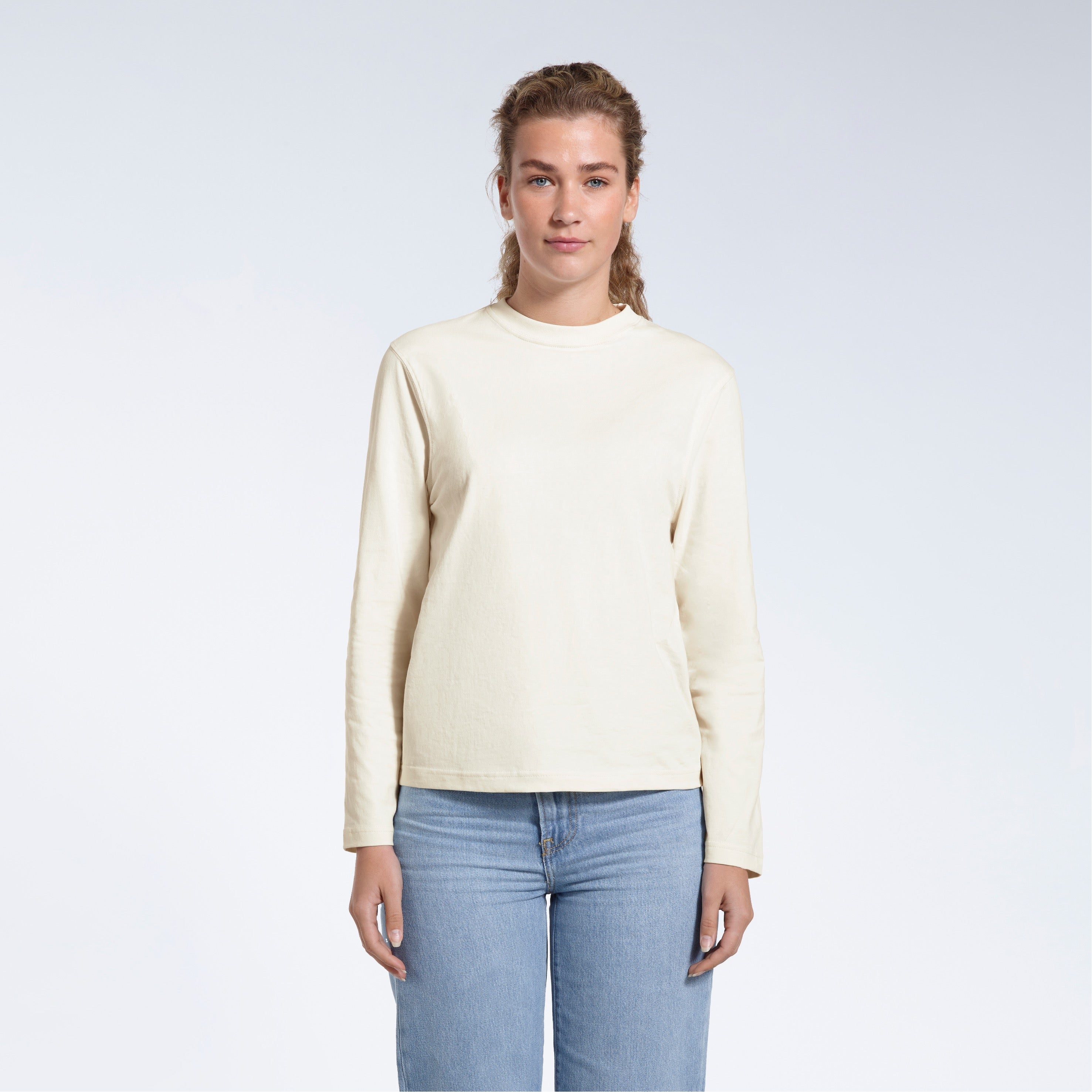 A woman standing front on with her arms by her sides, modelling a plain ecru long sleeve organic cotton t shirt.