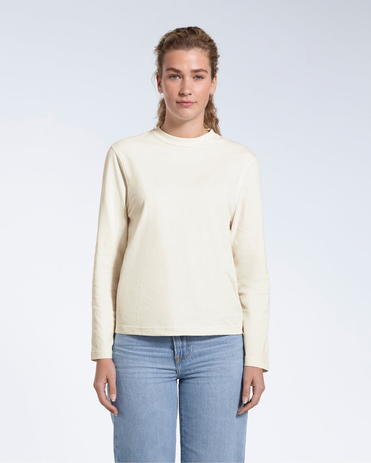 A woman standing front on with her arms by her sides, modelling a plain ecru long sleeve organic cotton t shirt.