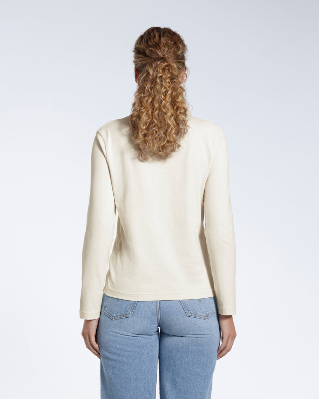 A woman facing away from the camera with her arms by her sides, modelling a plain ecru long sleeve organic cotton t shirt.