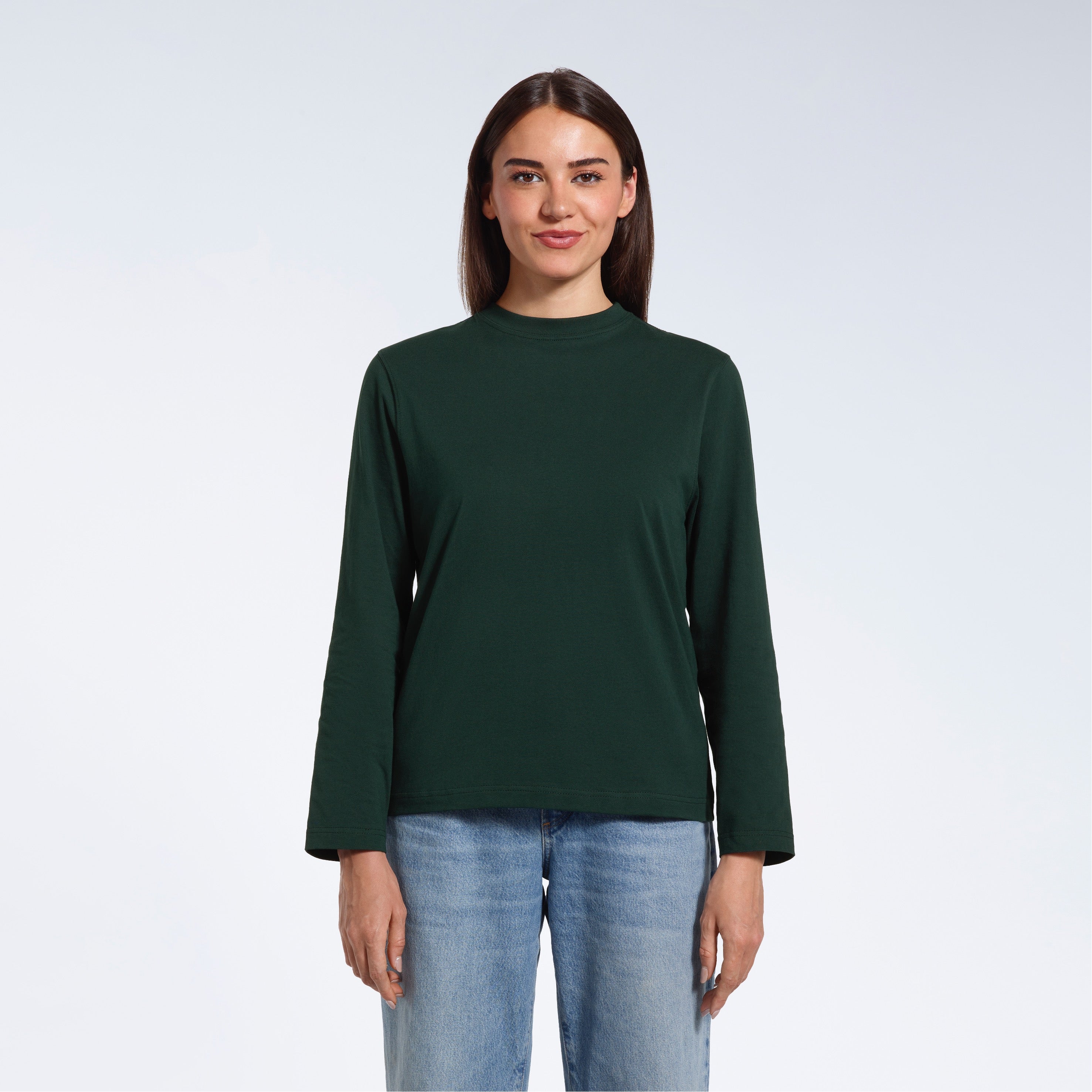 A woman standing front on with her arms by her sides, modelling a plain green long sleeve organic cotton t shirt.