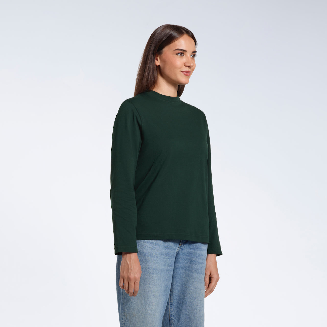 A woman looking away from the camera with her arms by her sides, modelling a plain green long sleeve organic cotton t shirt.