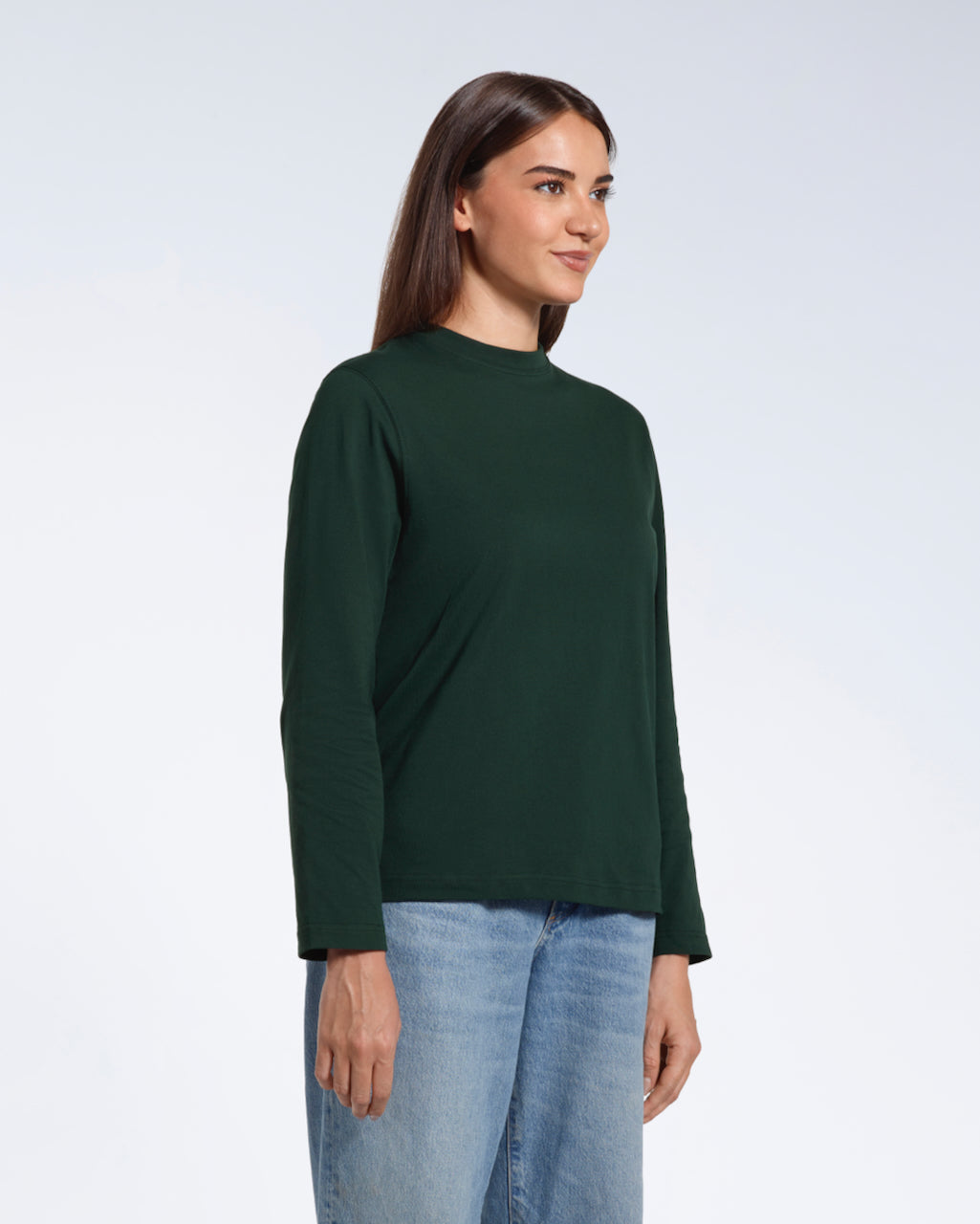A woman looking away from the camera with her arms by her sides, modelling a plain green long sleeve organic cotton t shirt.