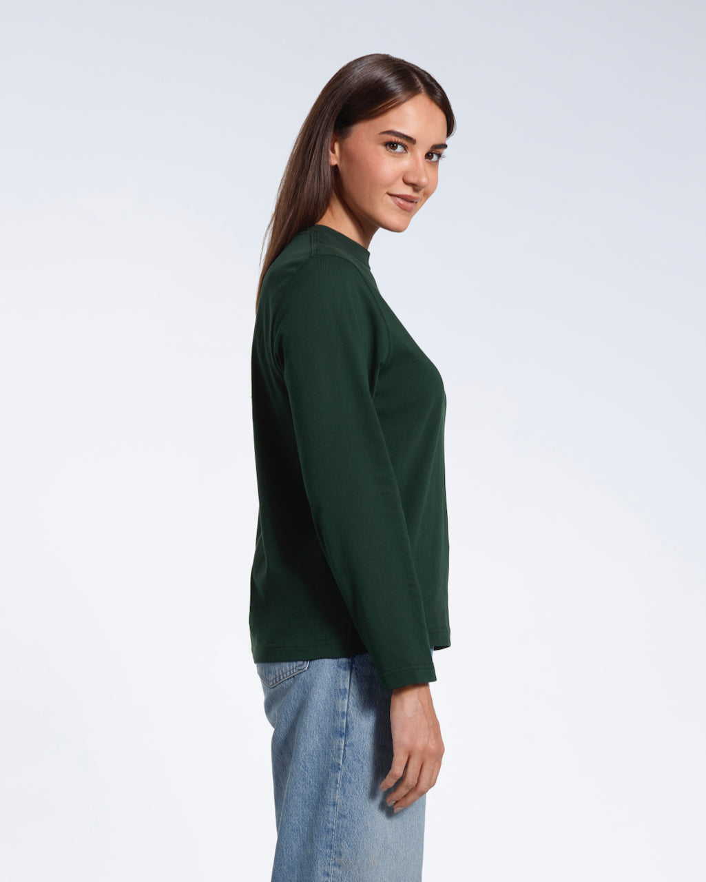 A woman facing side on looking at the camera, modelling a plain green long sleeve organic cotton t shirt.
