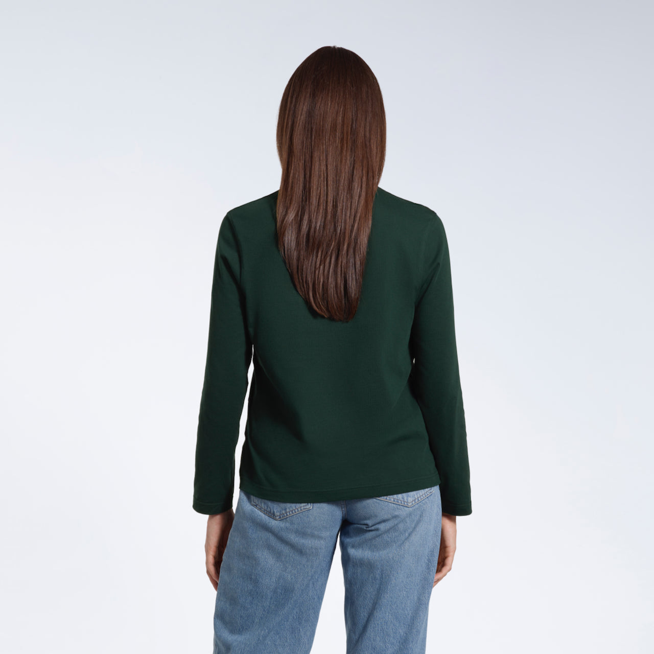 A woman facing away from the camera with her arms by her sides, modelling a plain green long sleeve organic cotton t shirt.