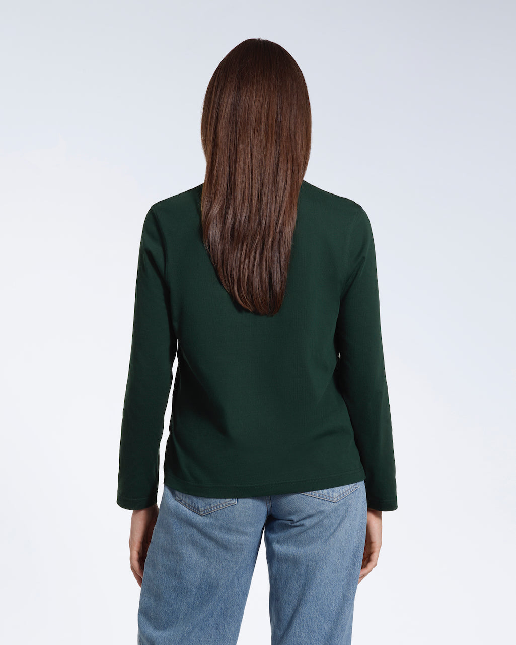 A woman facing away from the camera with her arms by her sides, modelling a plain green long sleeve organic cotton t shirt.