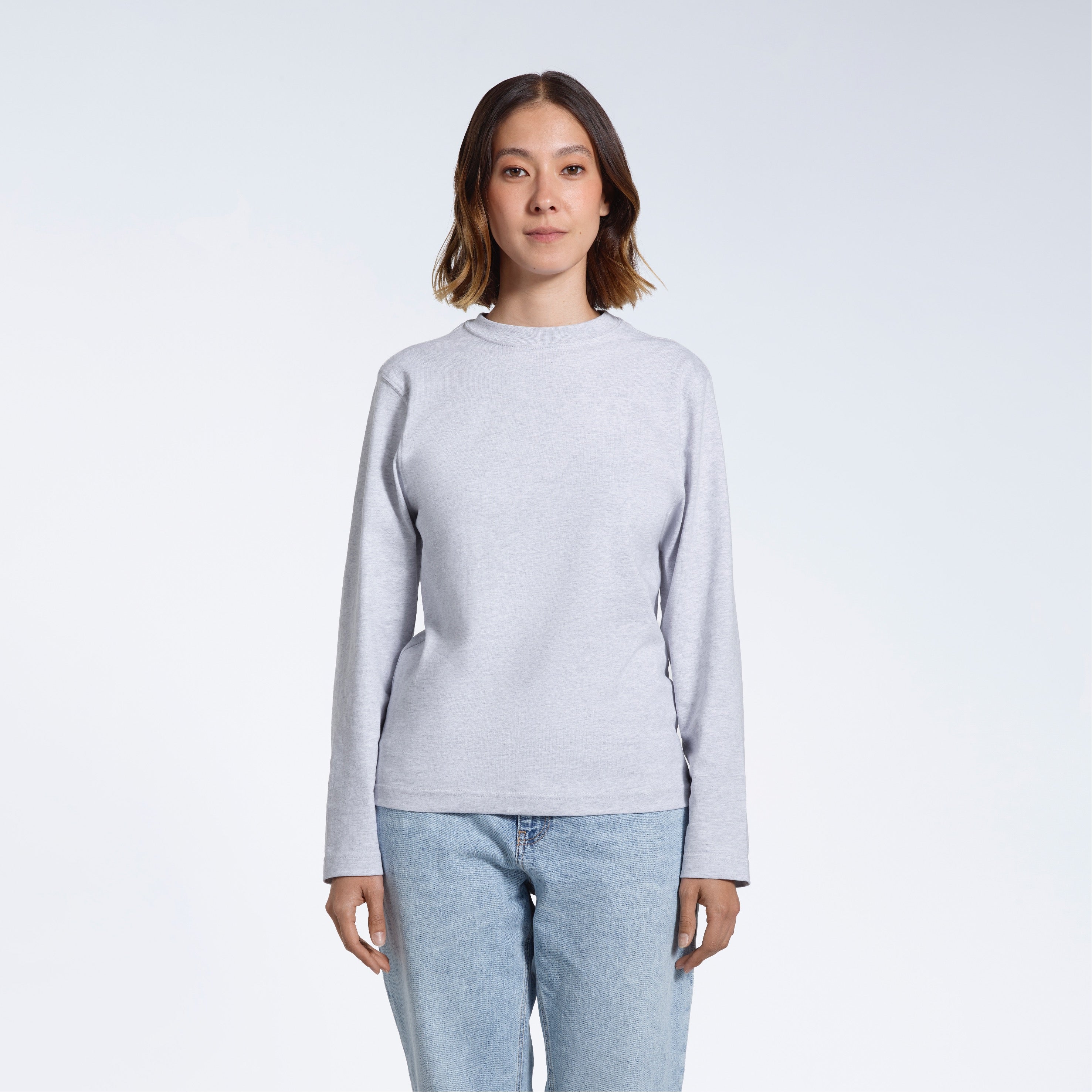 A woman standing front on with her arms by her sides, modelling a plain grey long sleeve organic cotton t shirt.