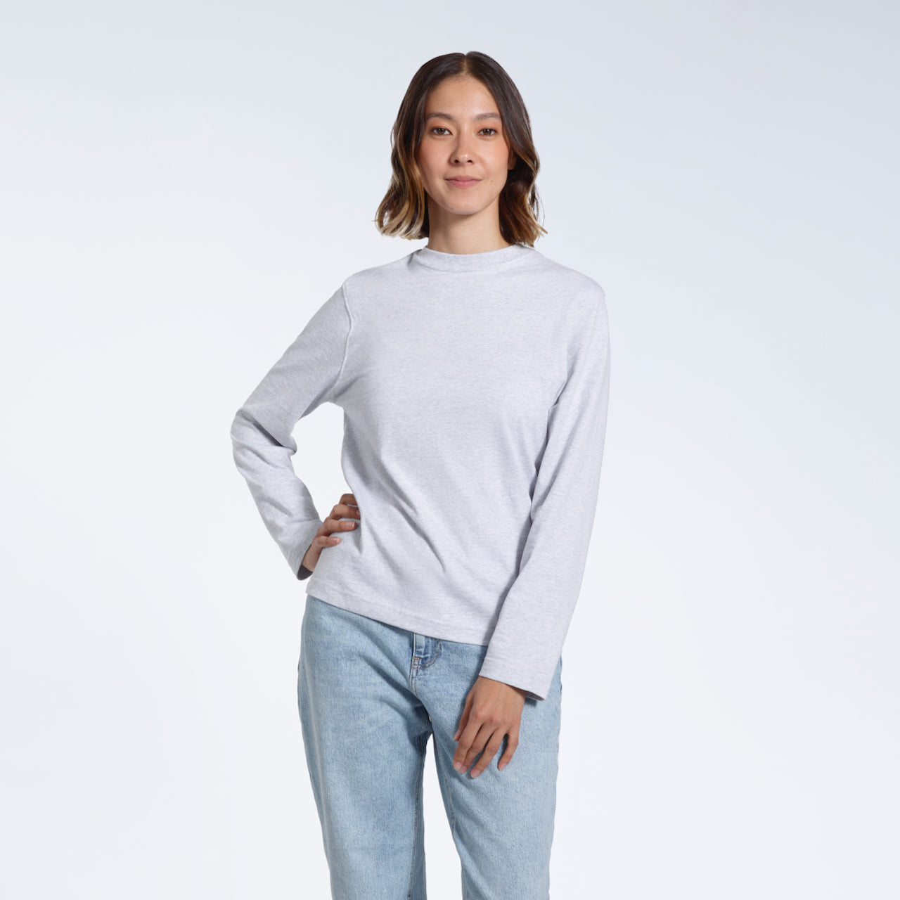 A woman looking into the camera with her hand on her hip, modelling a plain grey long sleeve organic cotton t shirt.
