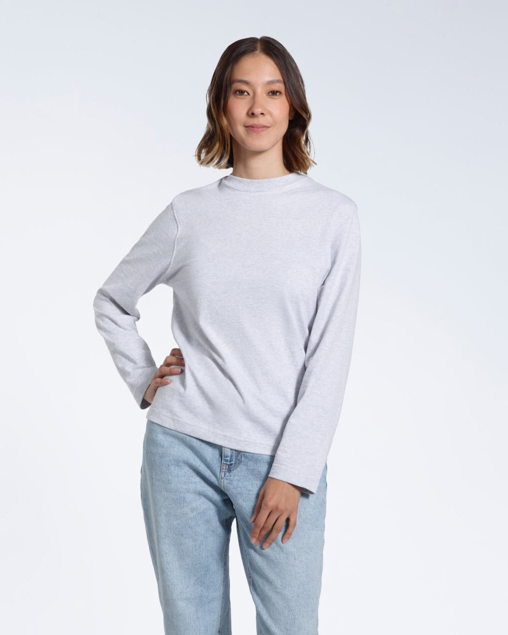 A woman looking into the camera with her hand on her hip, modelling a plain grey long sleeve organic cotton t shirt.