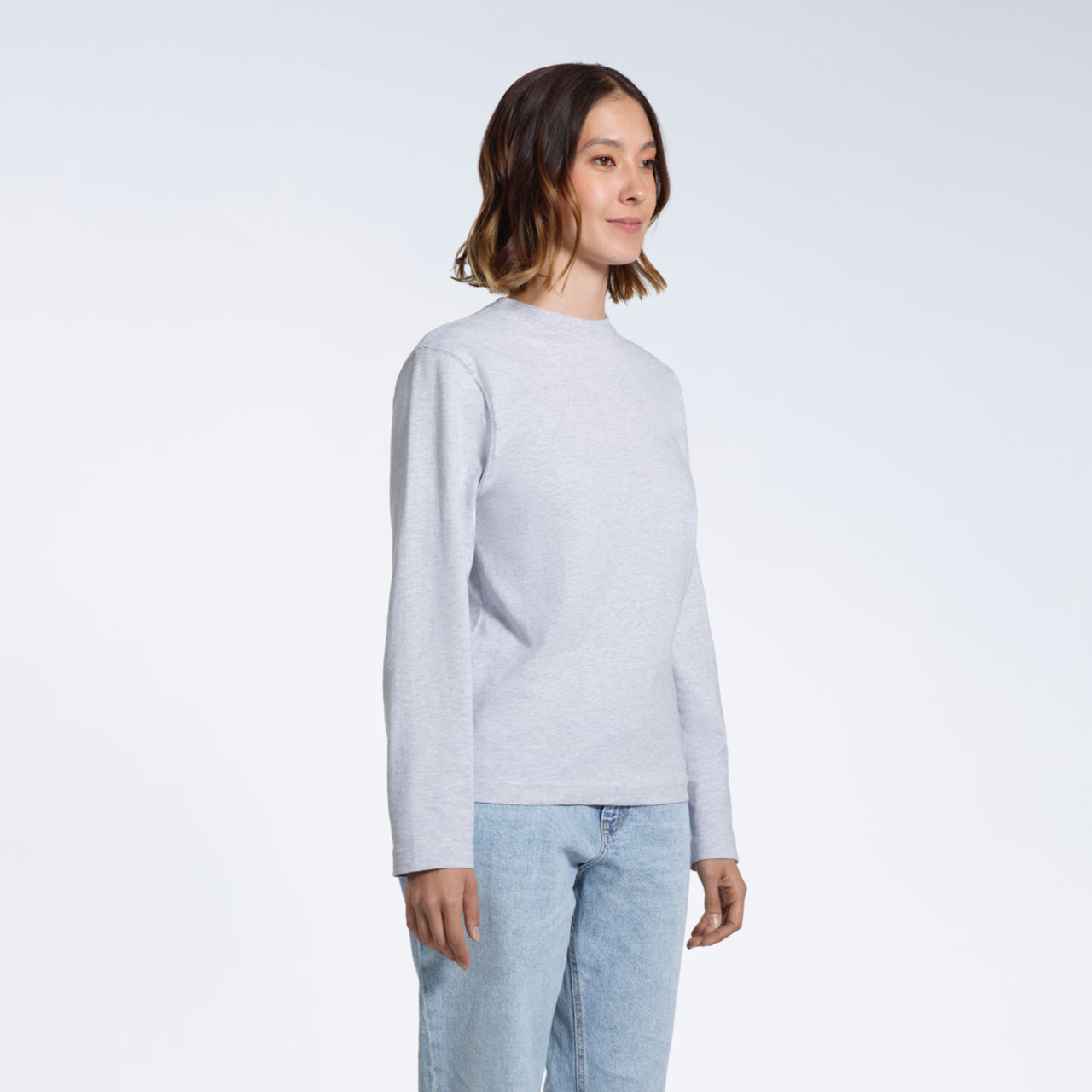 A woman looking away from the camera with her arms by her sides, modelling a plain grey long sleeve organic cotton t shirt.