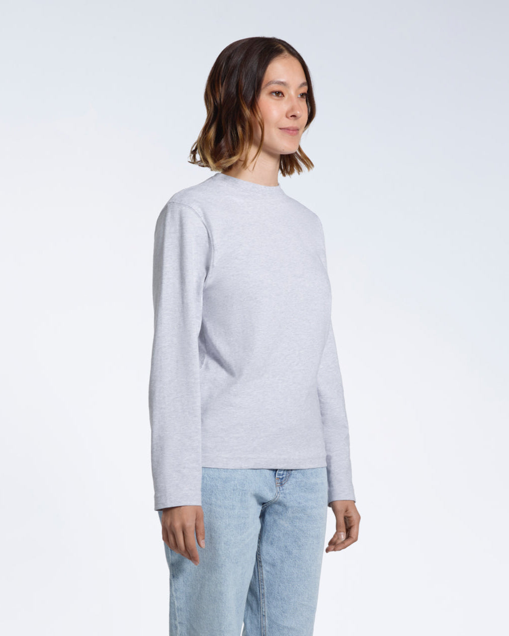 A woman looking away from the camera with her arms by her sides, modelling a plain grey long sleeve organic cotton t shirt.