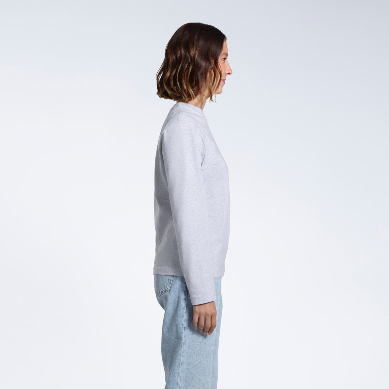 A woman facing side on with her arms by her sides, modelling a plain grey long sleeve organic cotton t shirt.