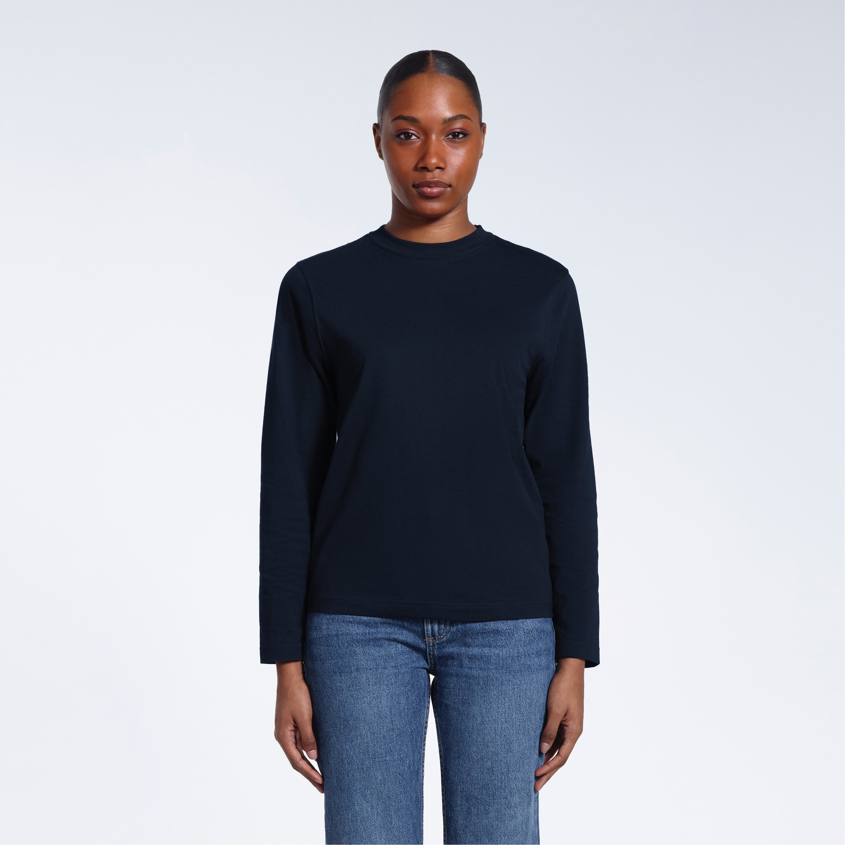 A woman standing front on with her arms by her sides, modelling a plain navy long sleeve organic cotton t shirt.
