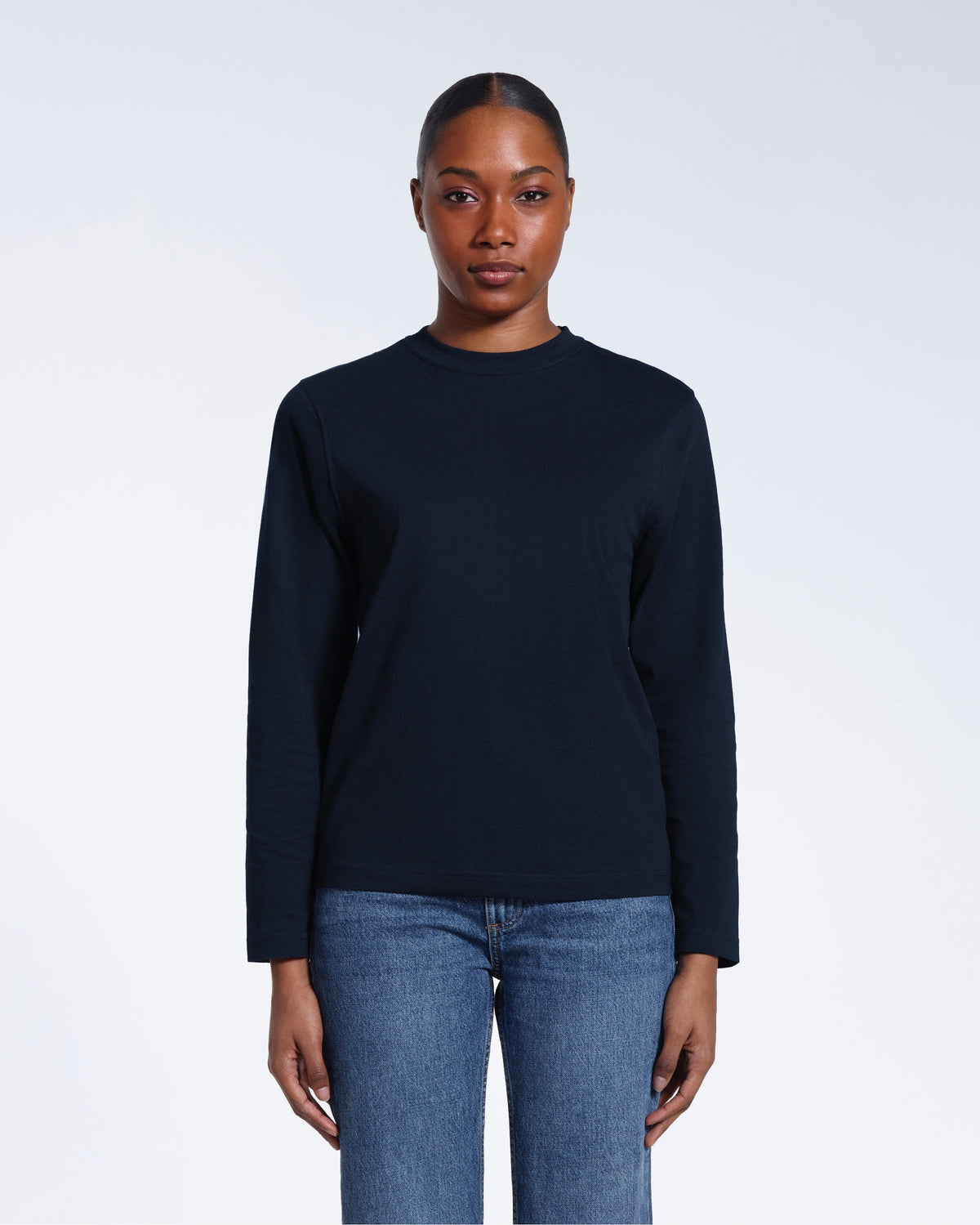 A woman standing front on with her arms by her sides, modelling a plain navy long sleeve organic cotton t shirt.