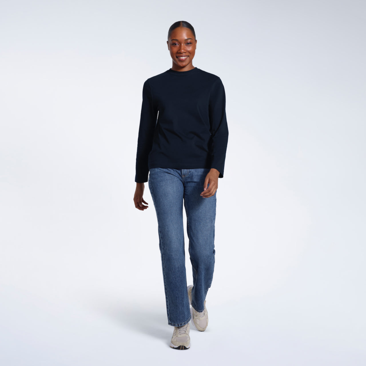A full body photo of a woman smiling into the camera, modelling a plain navy long sleeve organic cotton t shirt.