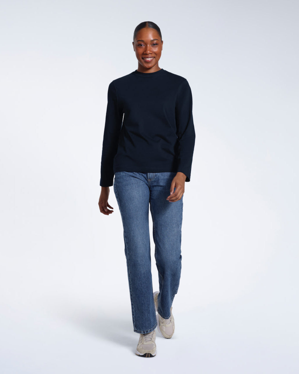 A full body photo of a woman smiling into the camera, modelling a plain navy long sleeve organic cotton t shirt.