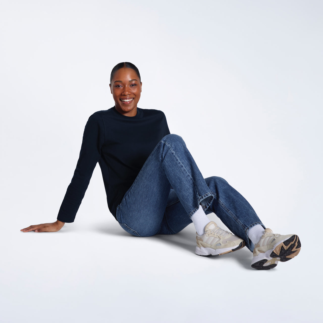 A woman sitting on the floor smiling, modelling a plain navy long sleeve organic cotton t shirt.
