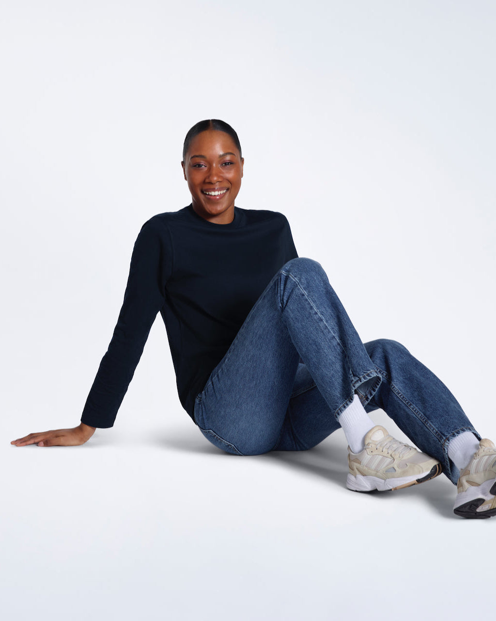A woman sitting on the floor smiling, modelling a plain navy long sleeve organic cotton t shirt.