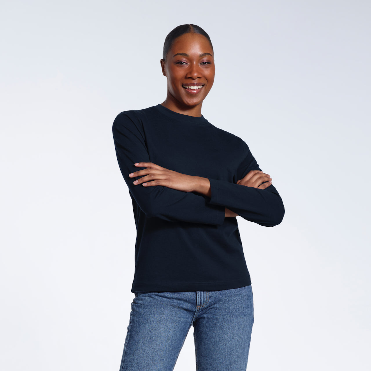 A woman smiling into the camera with her arms folded, modelling a plain navy long sleeve organic cotton t shirt.