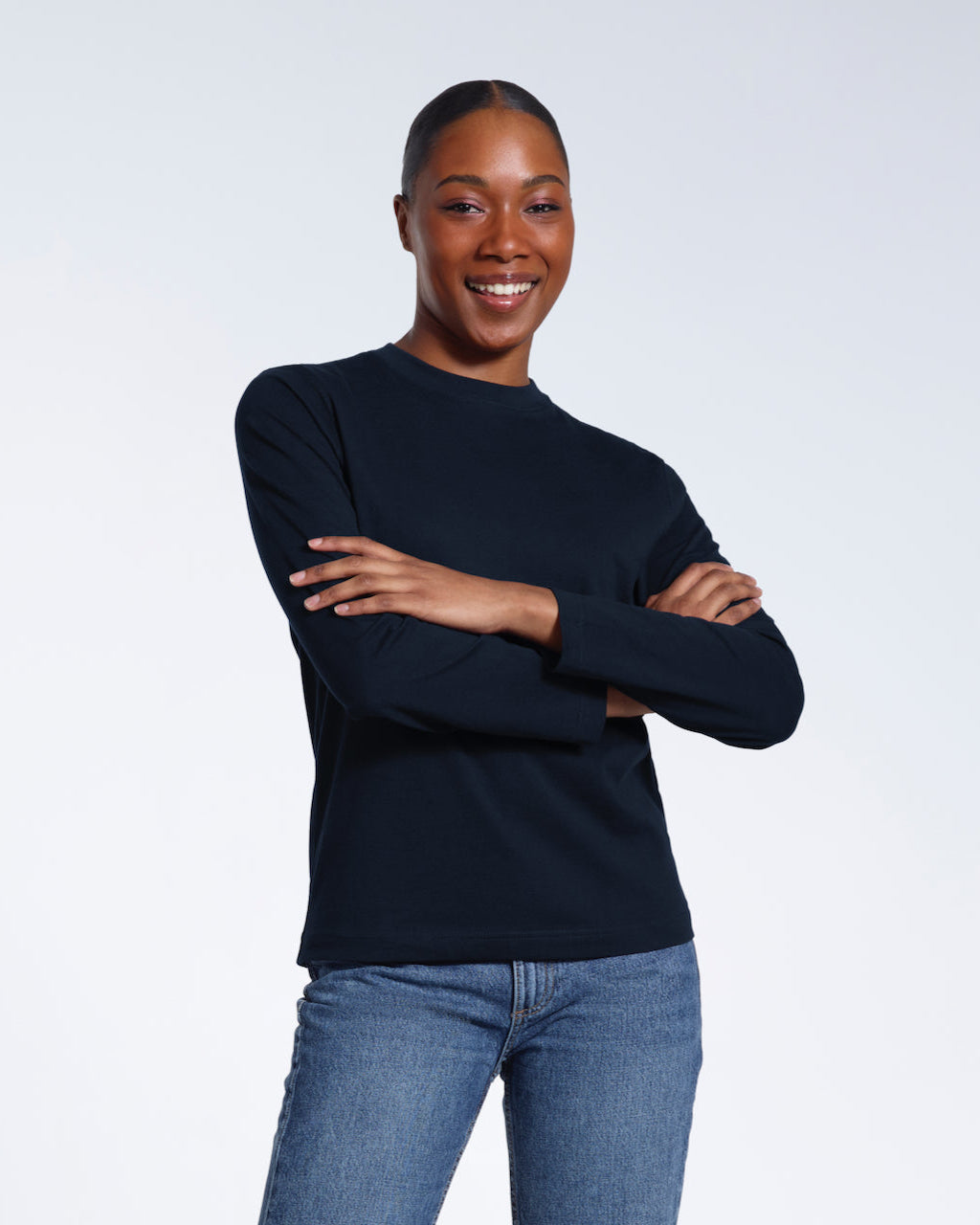 A woman smiling into the camera with her arms folded, modelling a plain navy long sleeve organic cotton t shirt.