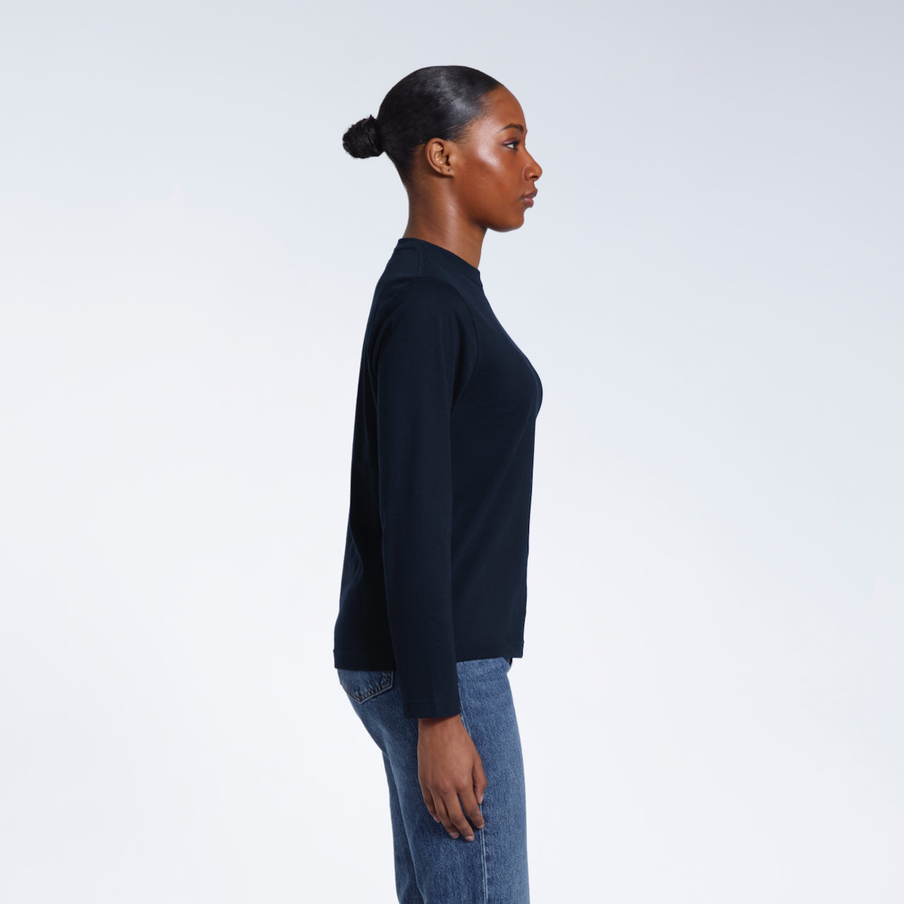 A woman facing side on with her arms by her sides, modelling a plain navy long sleeve organic cotton t shirt.