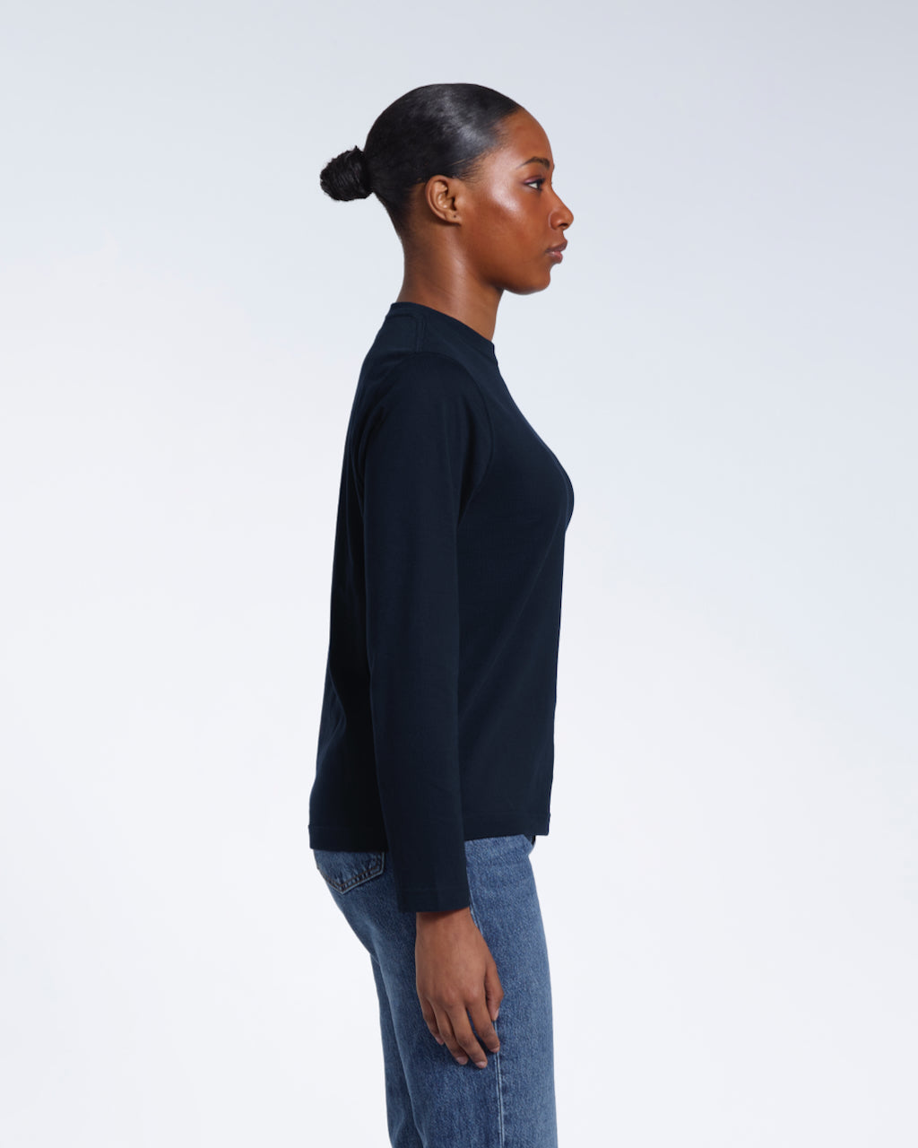 A woman facing side on with her arms by her sides, modelling a plain navy long sleeve organic cotton t shirt.