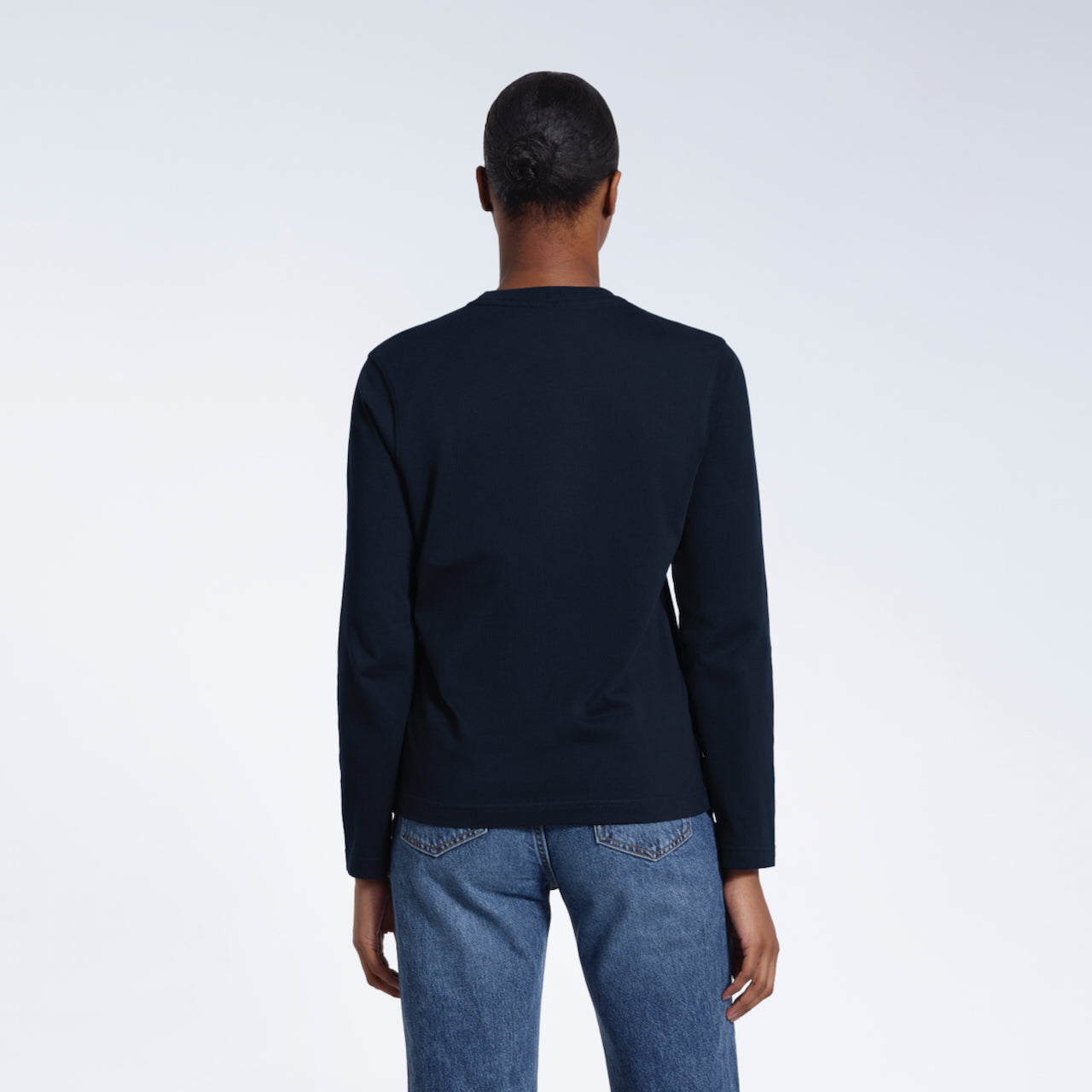 A woman facing away from the camera with her arms by her sides, modelling a plain navy long sleeve organic cotton t shirt.