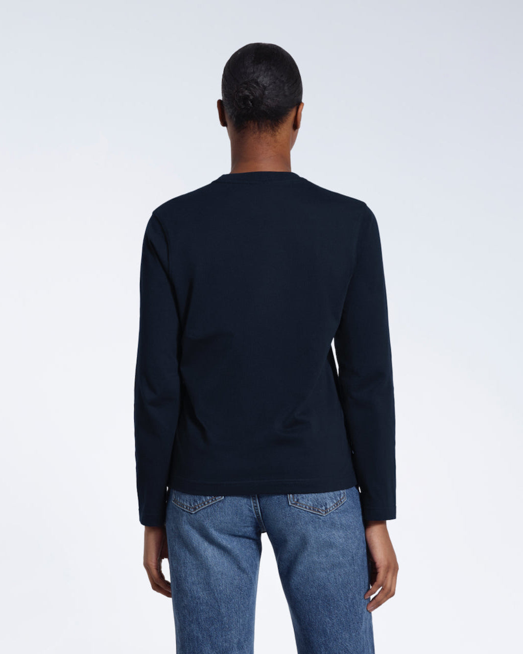 A woman facing away from the camera with her arms by her sides, modelling a plain navy long sleeve organic cotton t shirt.