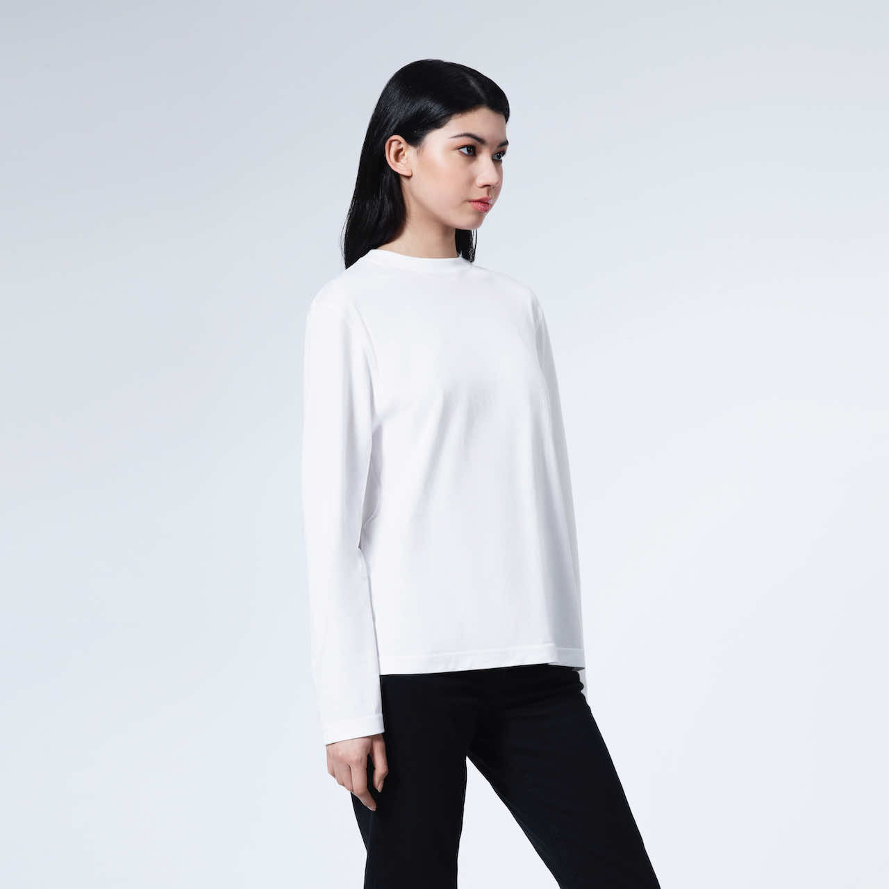 A woman looking away from the camera with her arms by her sides, modelling a plain white long sleeve organic cotton t shirt.