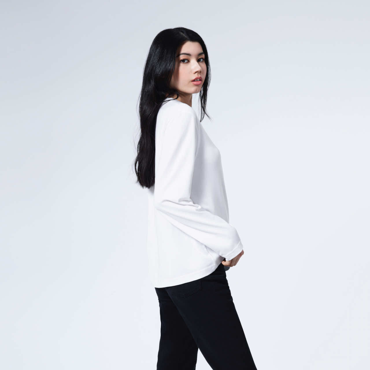 A woman facing side looking back at the camera, modelling a plain white long sleeve organic cotton t shirt.