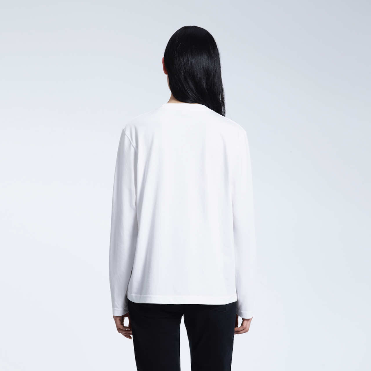 A woman facing away from the camera with her arms by her sides, modelling a plain white long sleeve organic cotton t shirt.