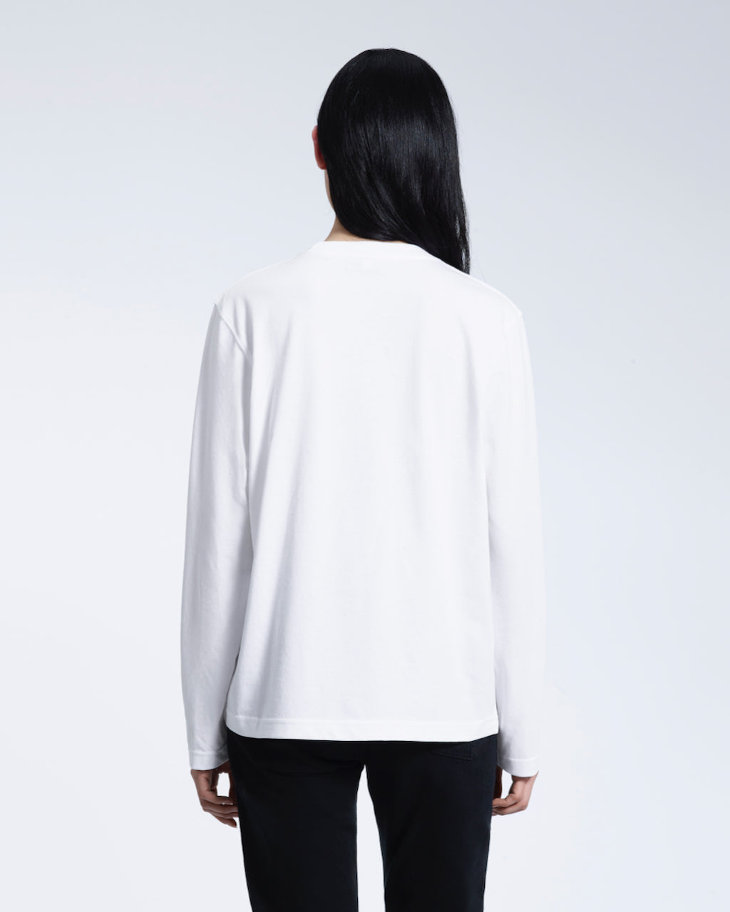 A woman facing away from the camera with her arms by her sides, modelling a plain white long sleeve organic cotton t shirt.