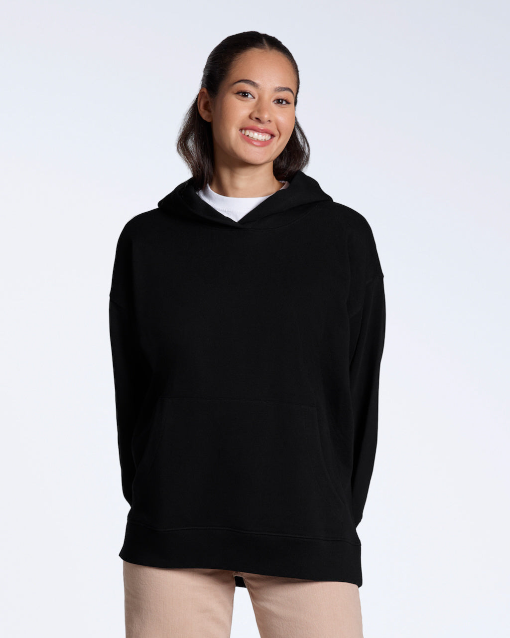 A woman smiling into the camera, modelling a plain black, oversized, organic cotton hoodie.
