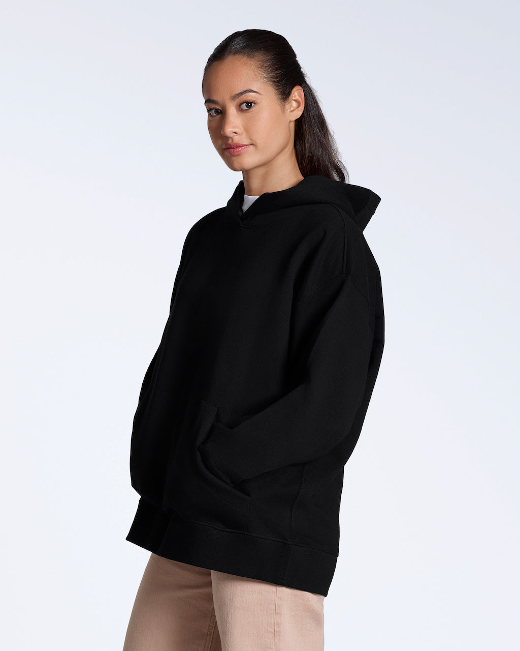 A woman facing side on looking back at the camera, modelling a plain black, oversized, organic cotton hoodie.
